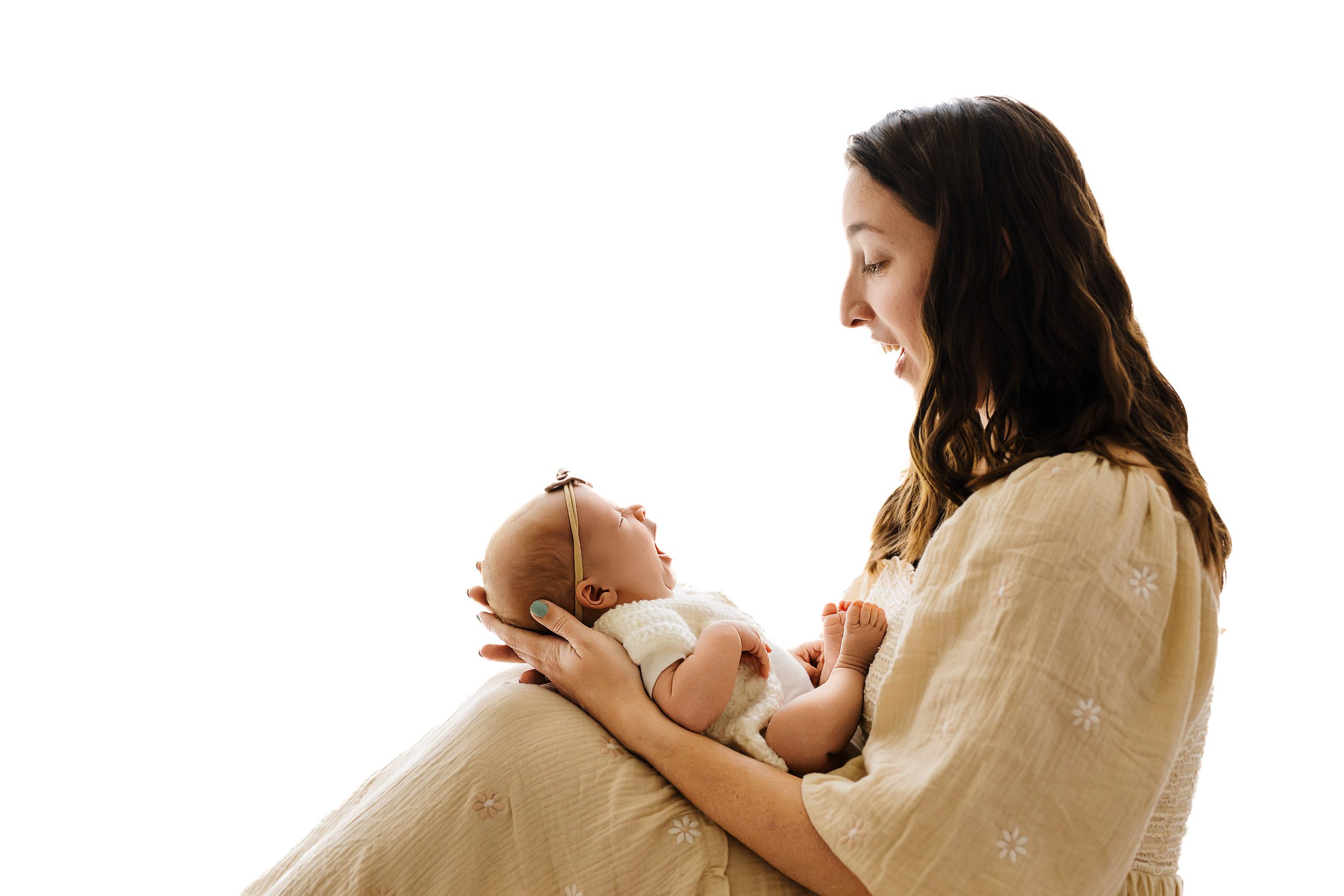 a backlit phot of a new mom holding her baby girl and smiling down at her as the baby yawns during a newborn family photoshoot