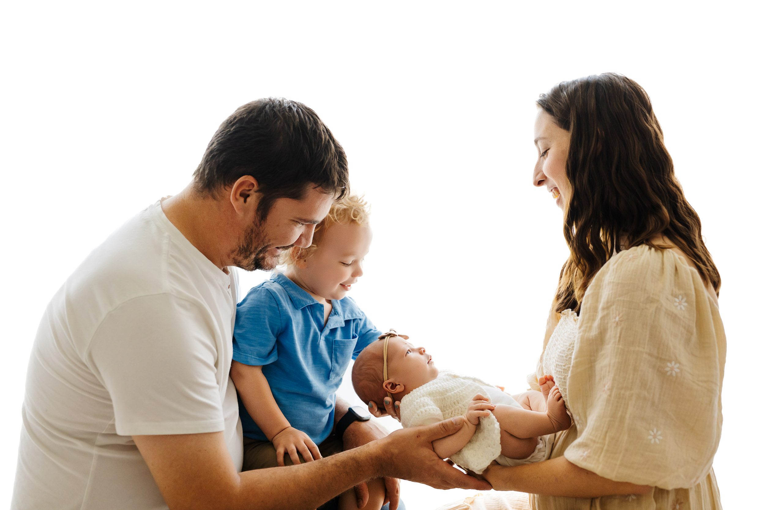 a backlit photo of a family of four sitting on a bench as they all smile at their new baby girl in mom's arms during a newborn family photoshoot