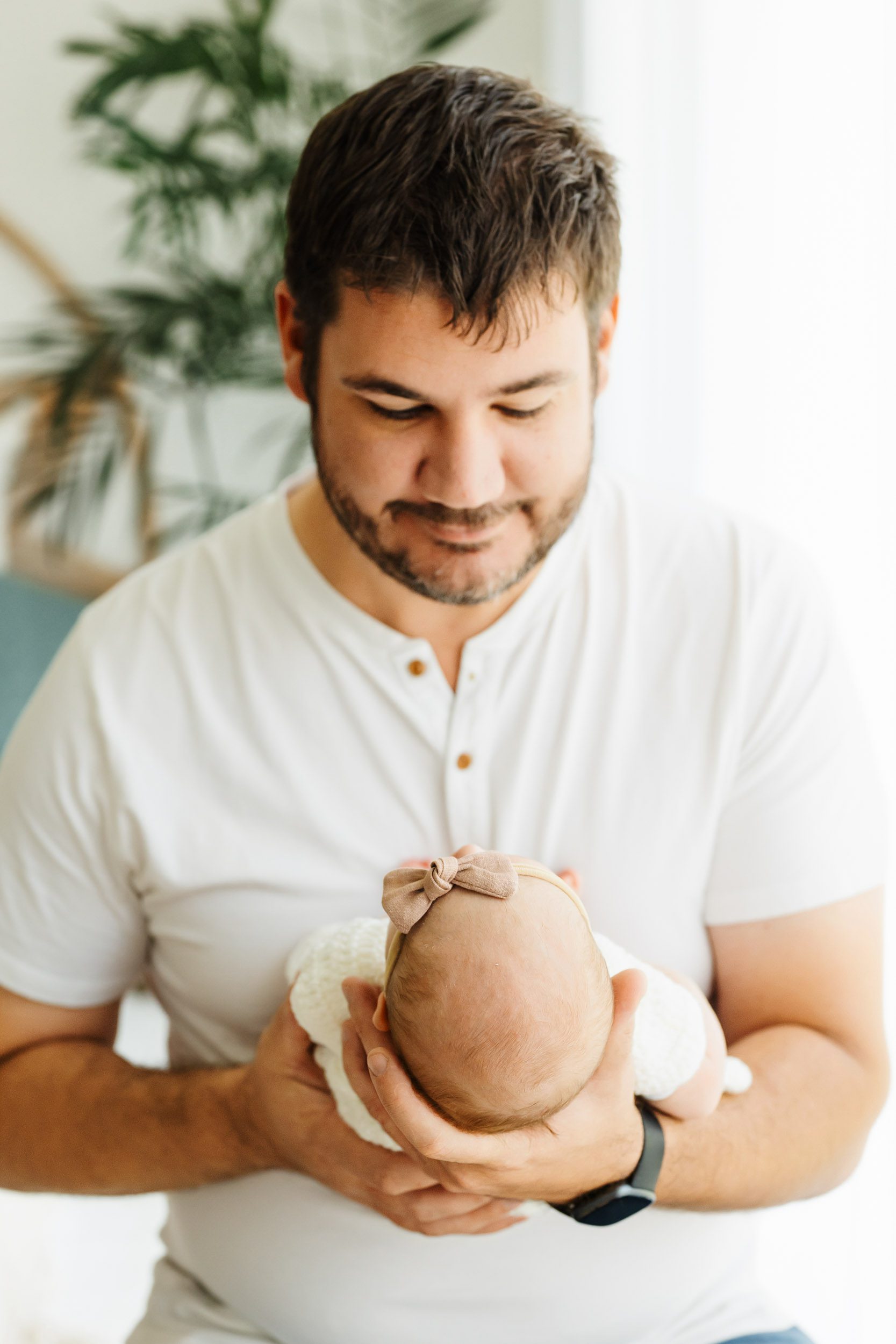 a new father holding his baby girl in his arms and gazing down at her during a newborn family photoshoot