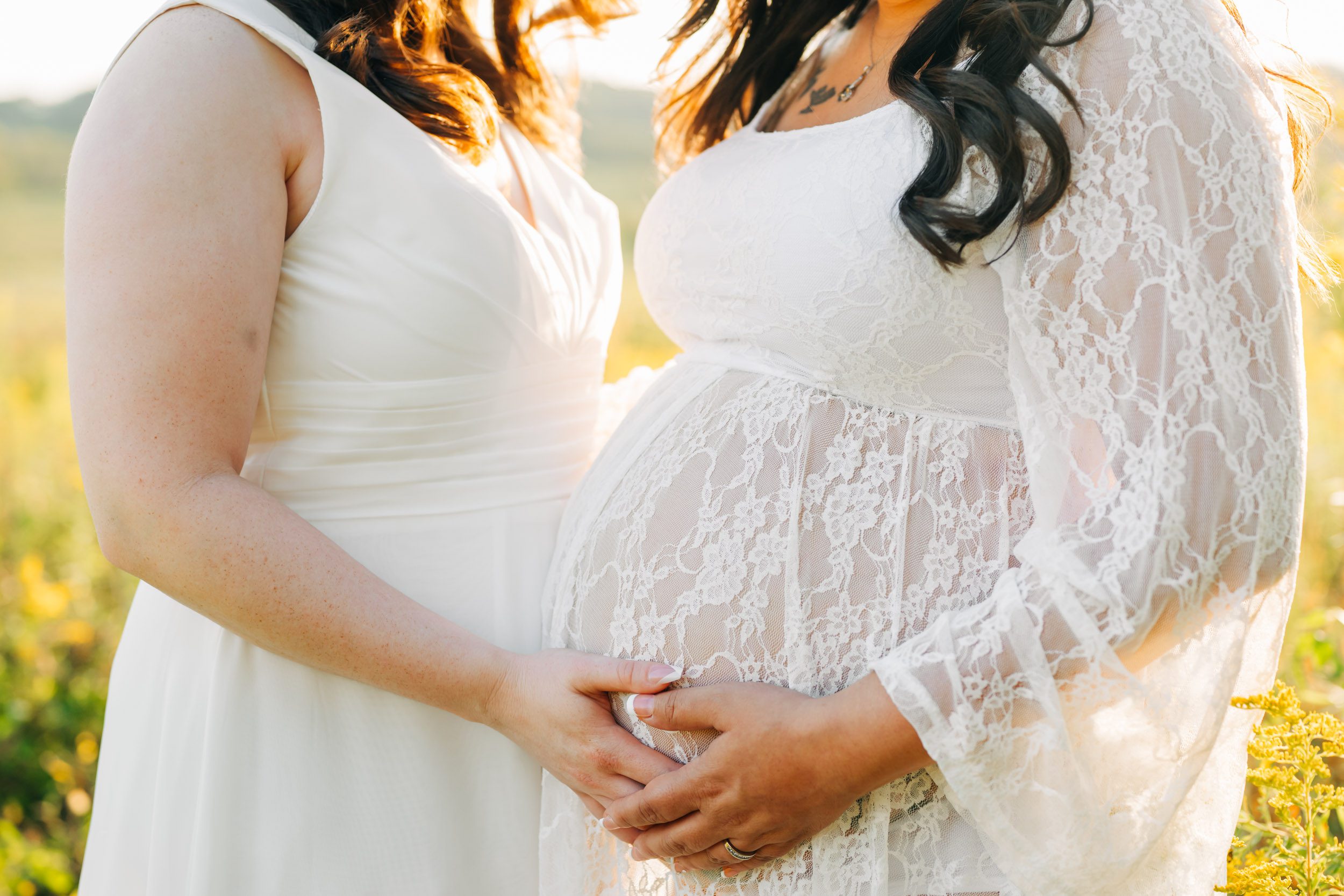 a close up photo of an expecting mom's belly as she and her wife both rest their hands on her belly during an LGBT maternity photo session