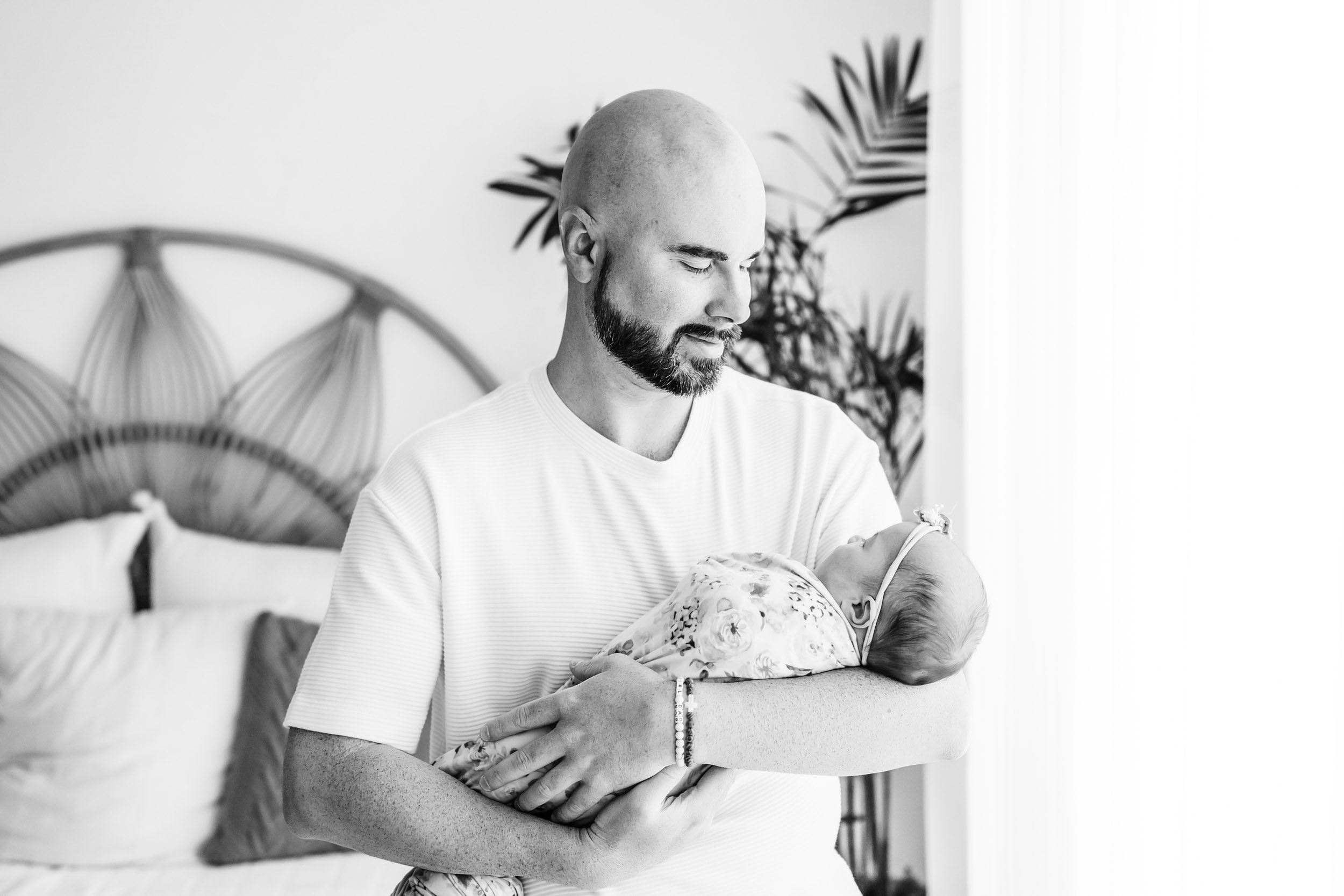 a black and white picture of a new dad cradling his baby girl in his arms and smiling down at her during a baby photography session