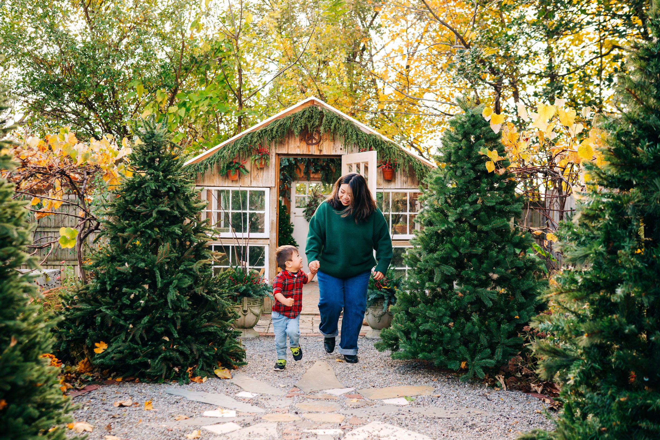 a little boy holding his mom's hand a they run past Christmas trees together during a holiday mini session
