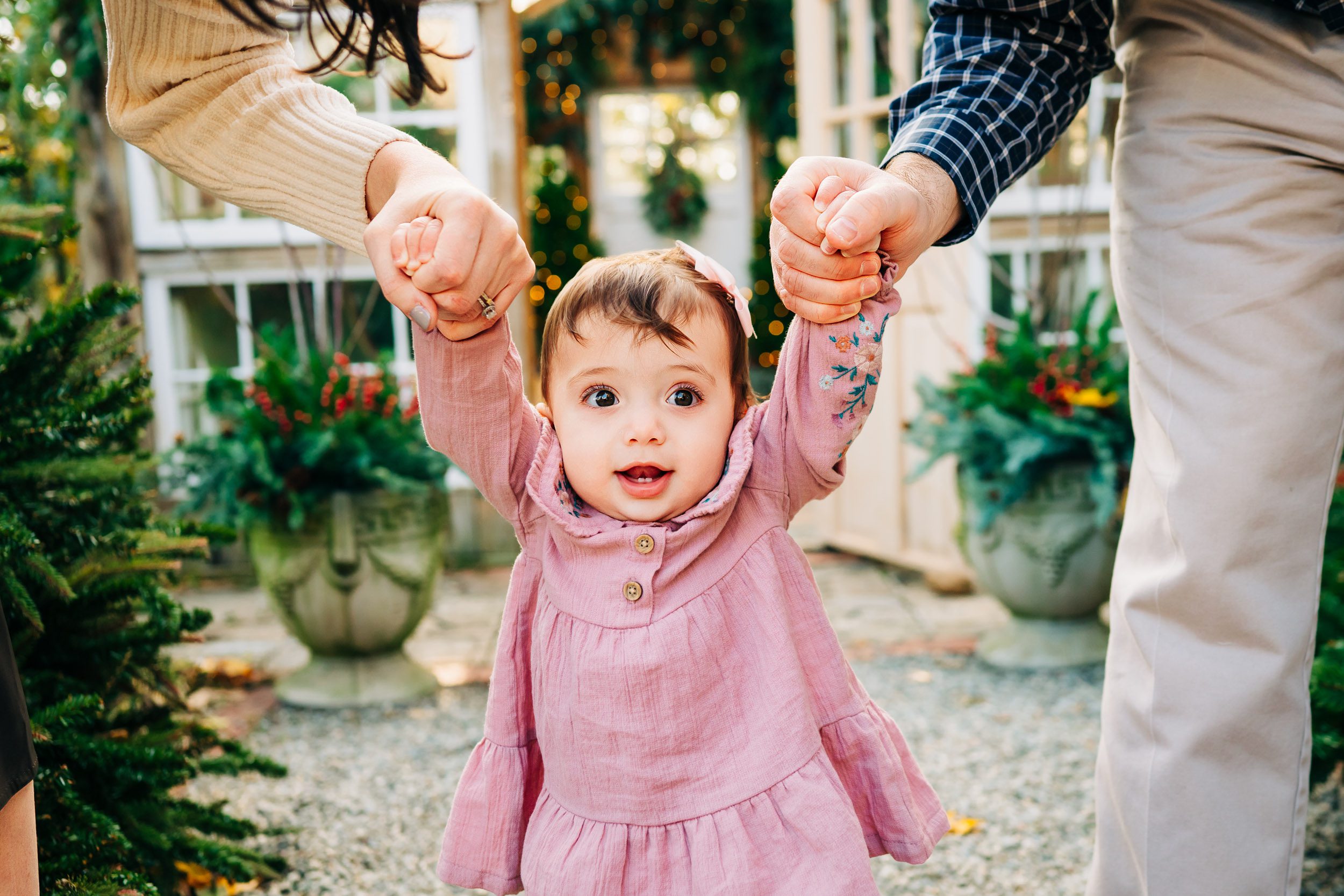 a young girl holding her parents hands and smiling to show off her two front teeth during a holiday mini session