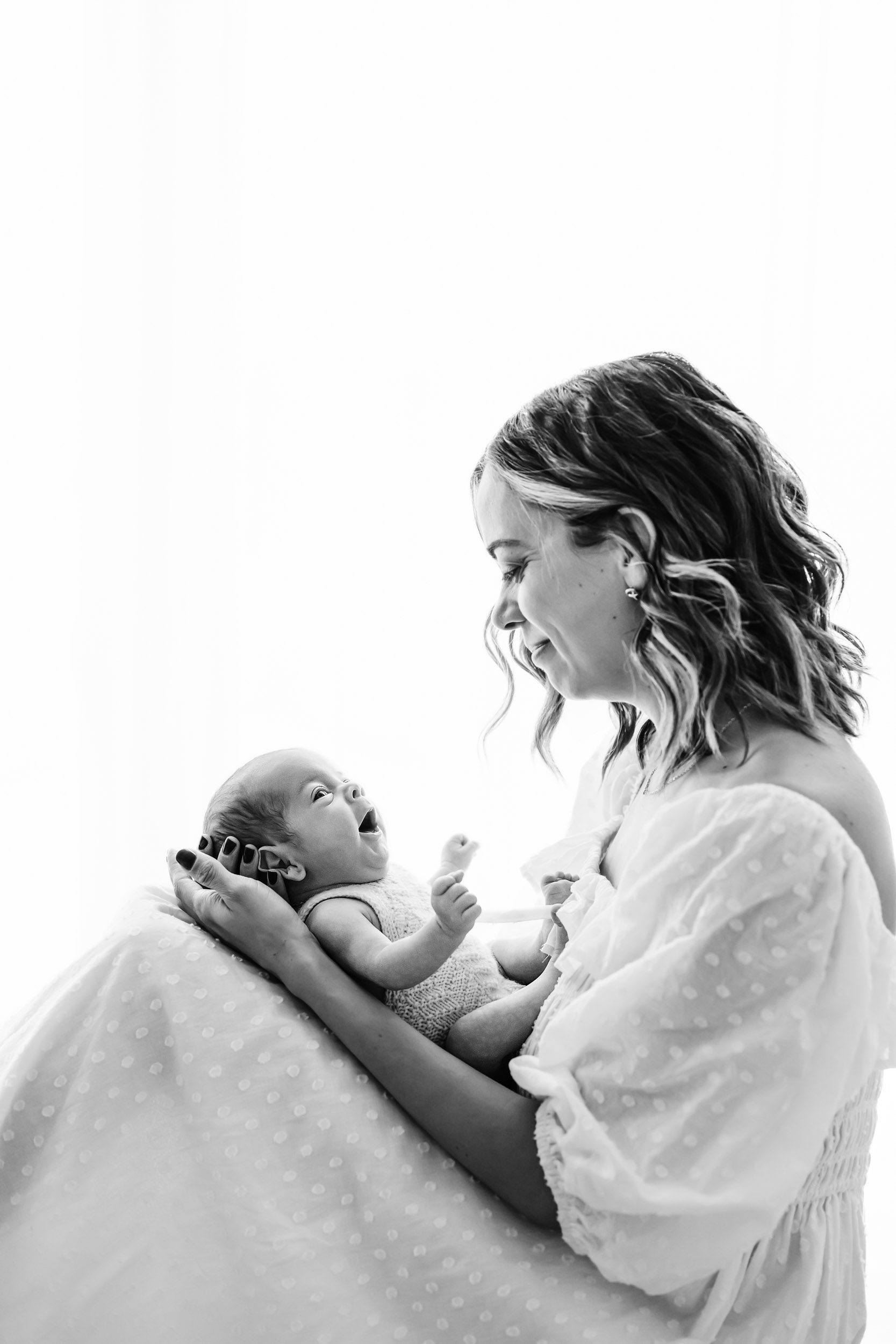 a black and white backlit photo of a mom holding her baby boy as he smiles up at her during a lifestyle newborn photography session
