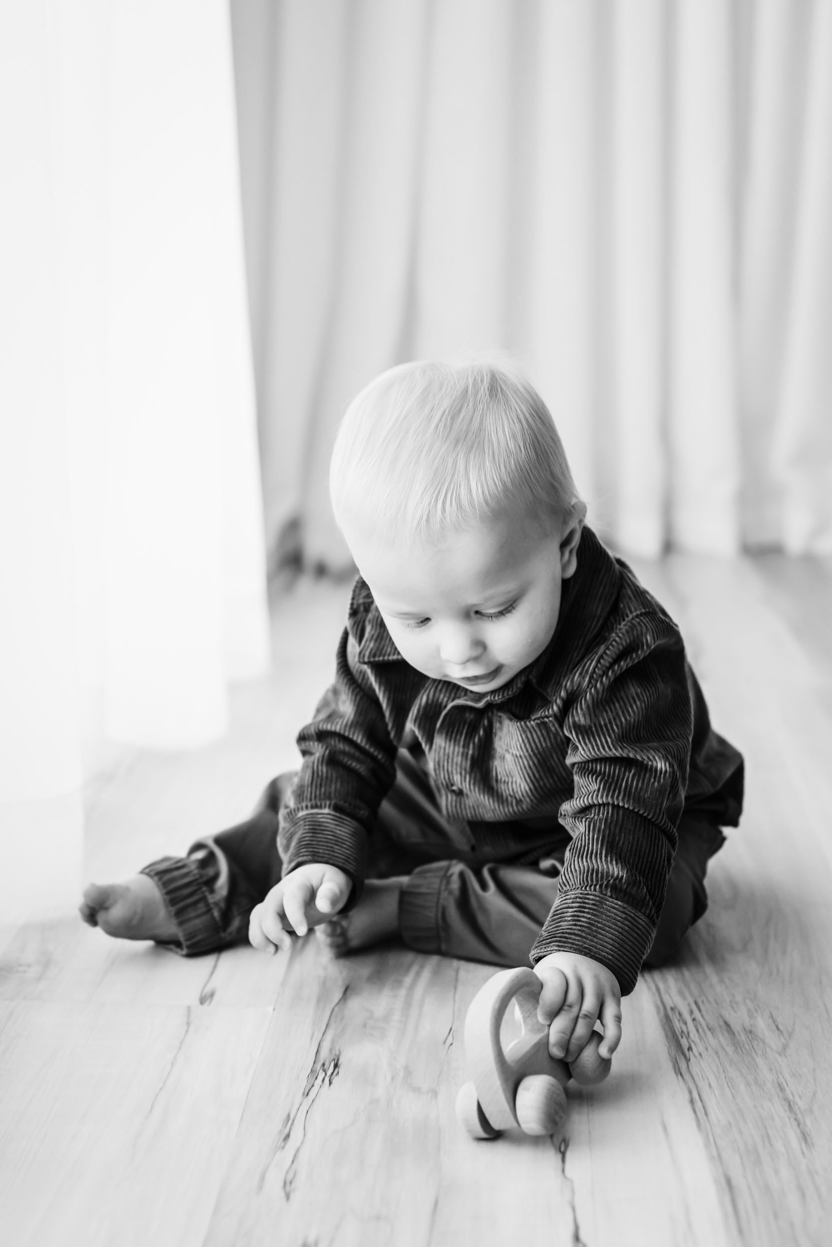 a black and white picture of a little boy sitting on the floor and playing with a toy car during his 1st birthday pictures