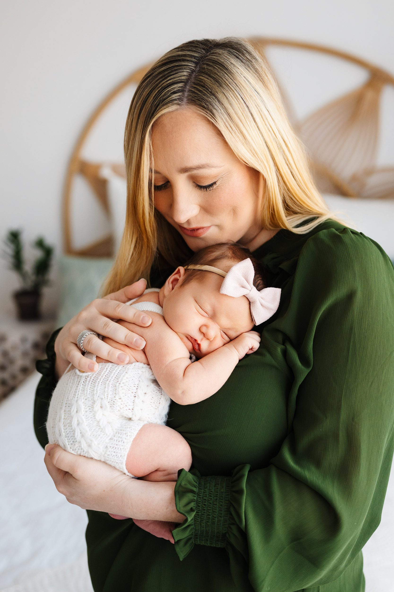 a new mom holding her newborn baby girl cuddled up against her chest and smiling down at her as the baby sleeps peacefully during a lifestyle newborn photoshoot