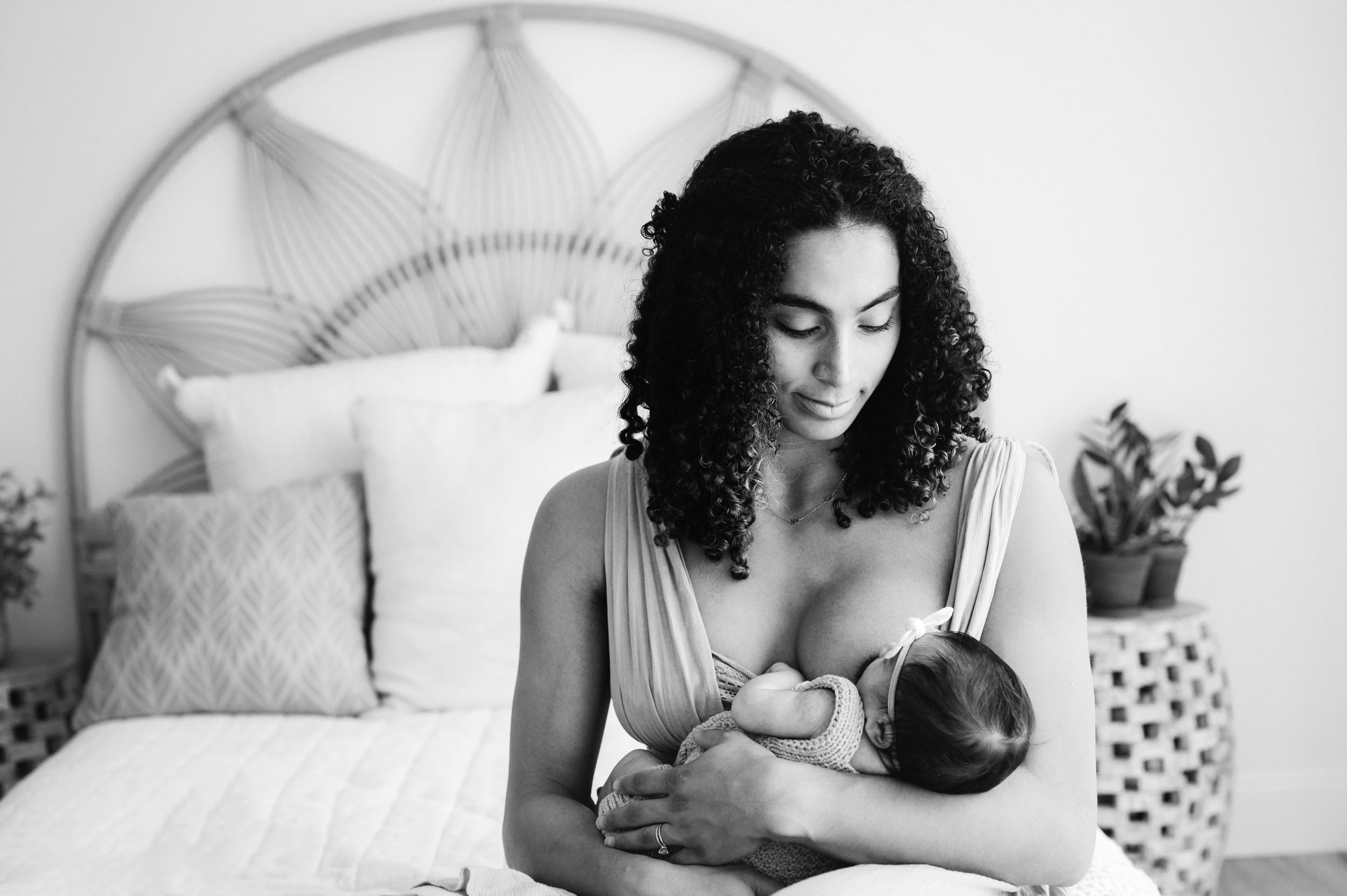 a black and white picture of a new mom sitting on a bed nursing her baby girl during a lifestyle newborn photoshoot