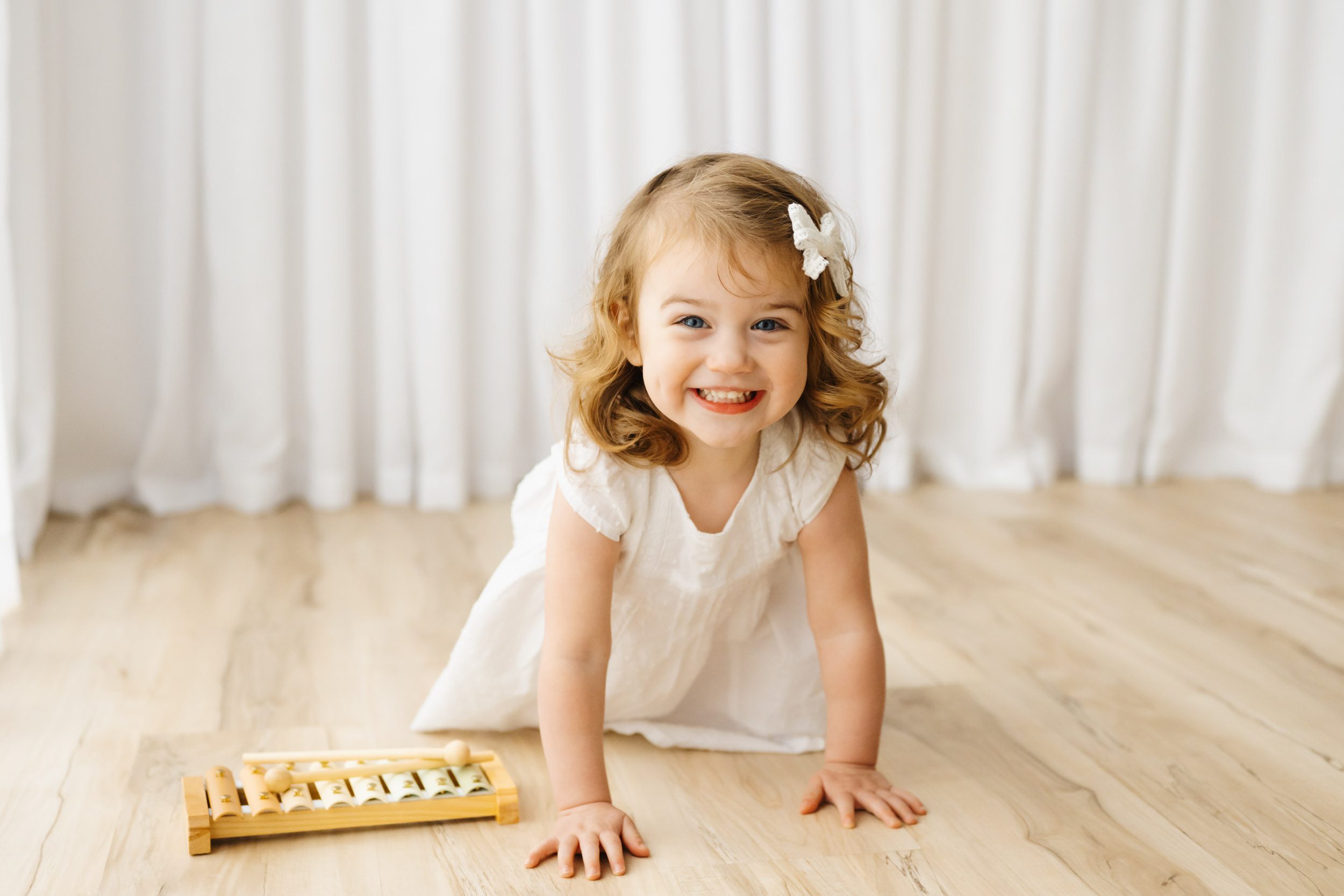 a little girl crawling across the floor and looking directly at the camera with a huge smile on her face during a 2nd birthday photoshoot