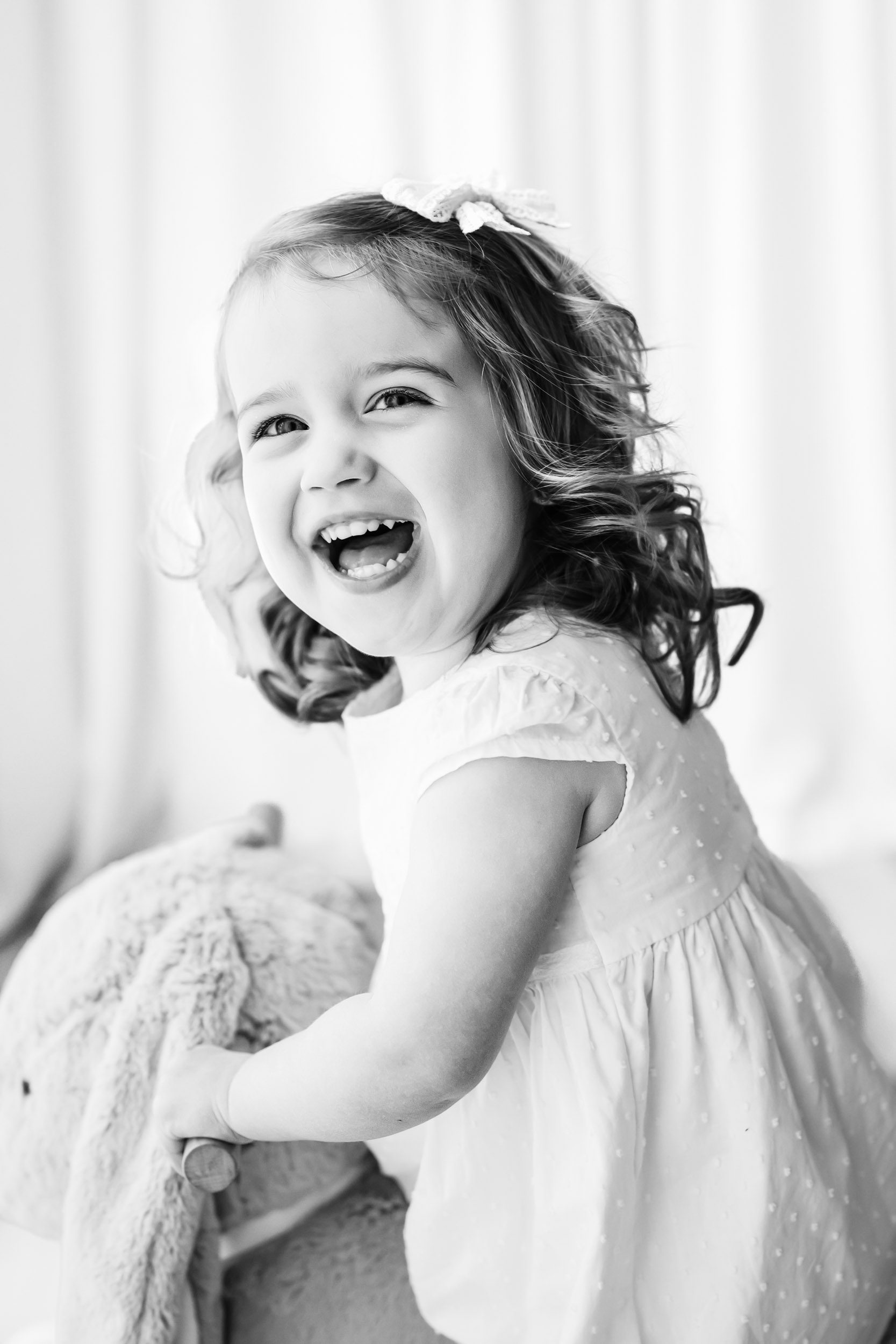 a black and white picture of a little girl riding a bunny rocker toy and looking at the camera with a huge smile on her face during a 2nd birthday photoshoot
