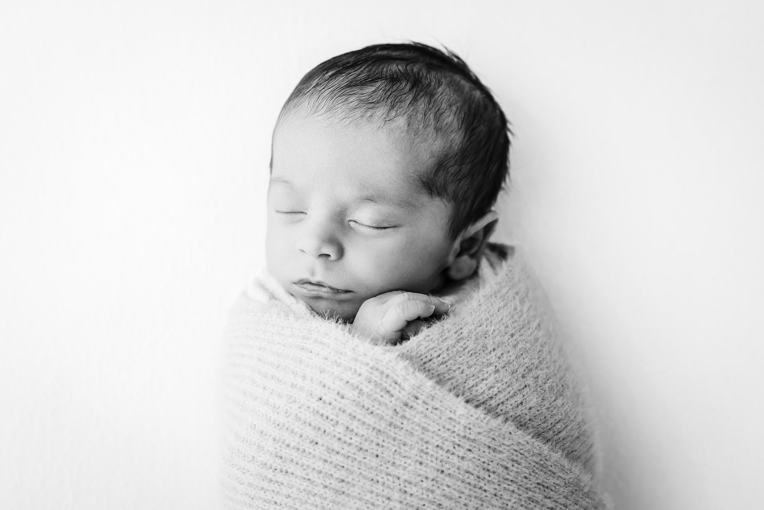 a black and white photo of a baby boy wrapped in a fuzzy ribbed blanket sleeping peacefully during an organic newborn photography session