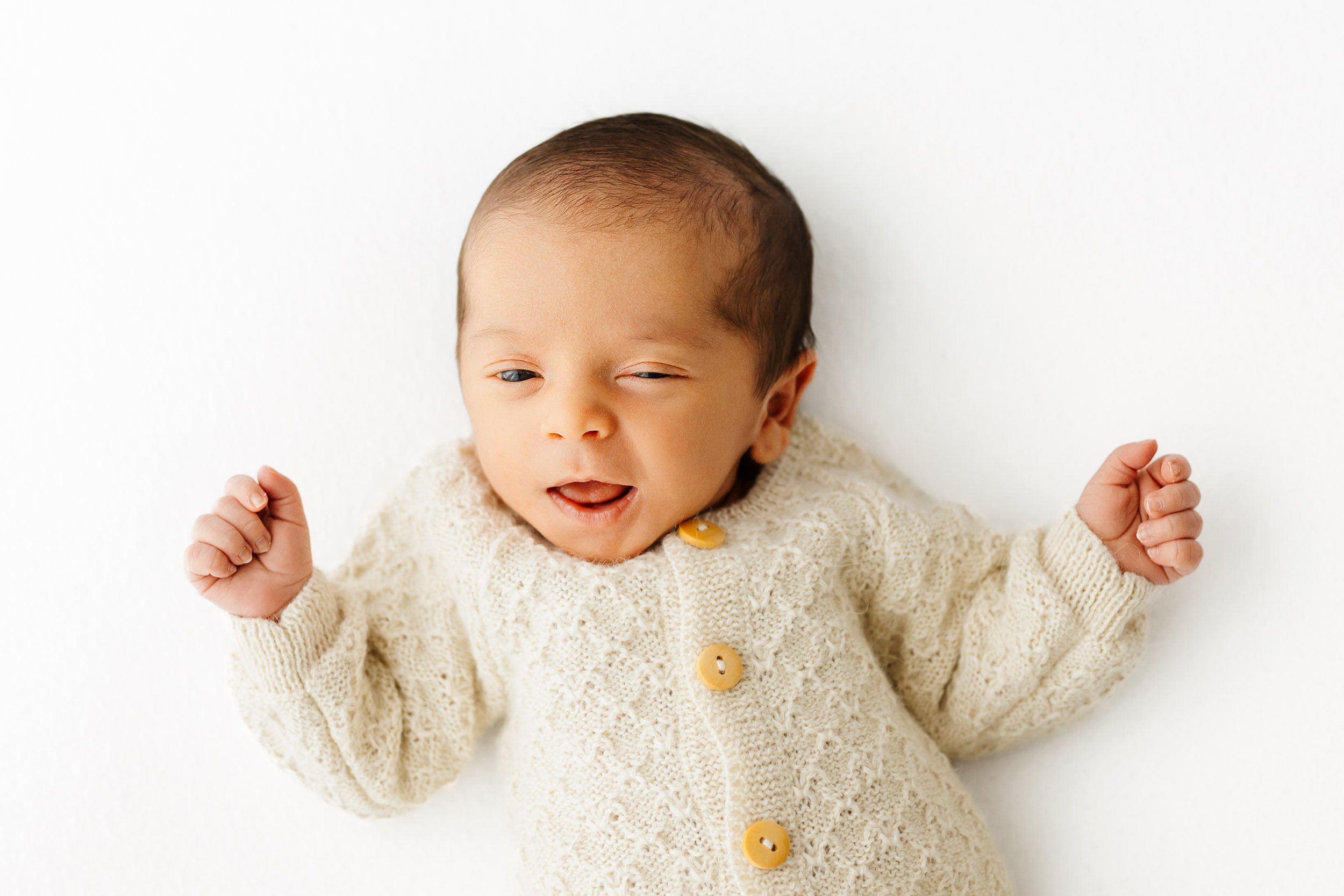 a baby boy wearing a long sleeve textured romper squinting his eyes and smiling up at the camera during an organic newborn photography session