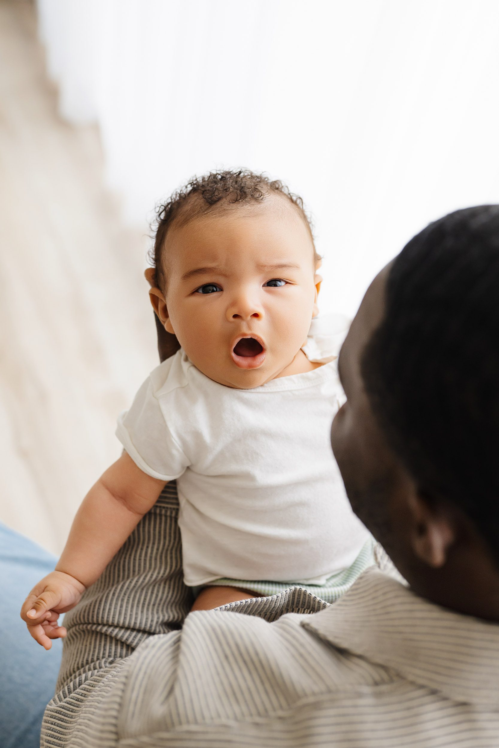 a picture taken from above of a dad holding his baby boy in his arms as the baby look at the camera and opens his mouth to yawn during a King of Prussia newborn photoshoot
