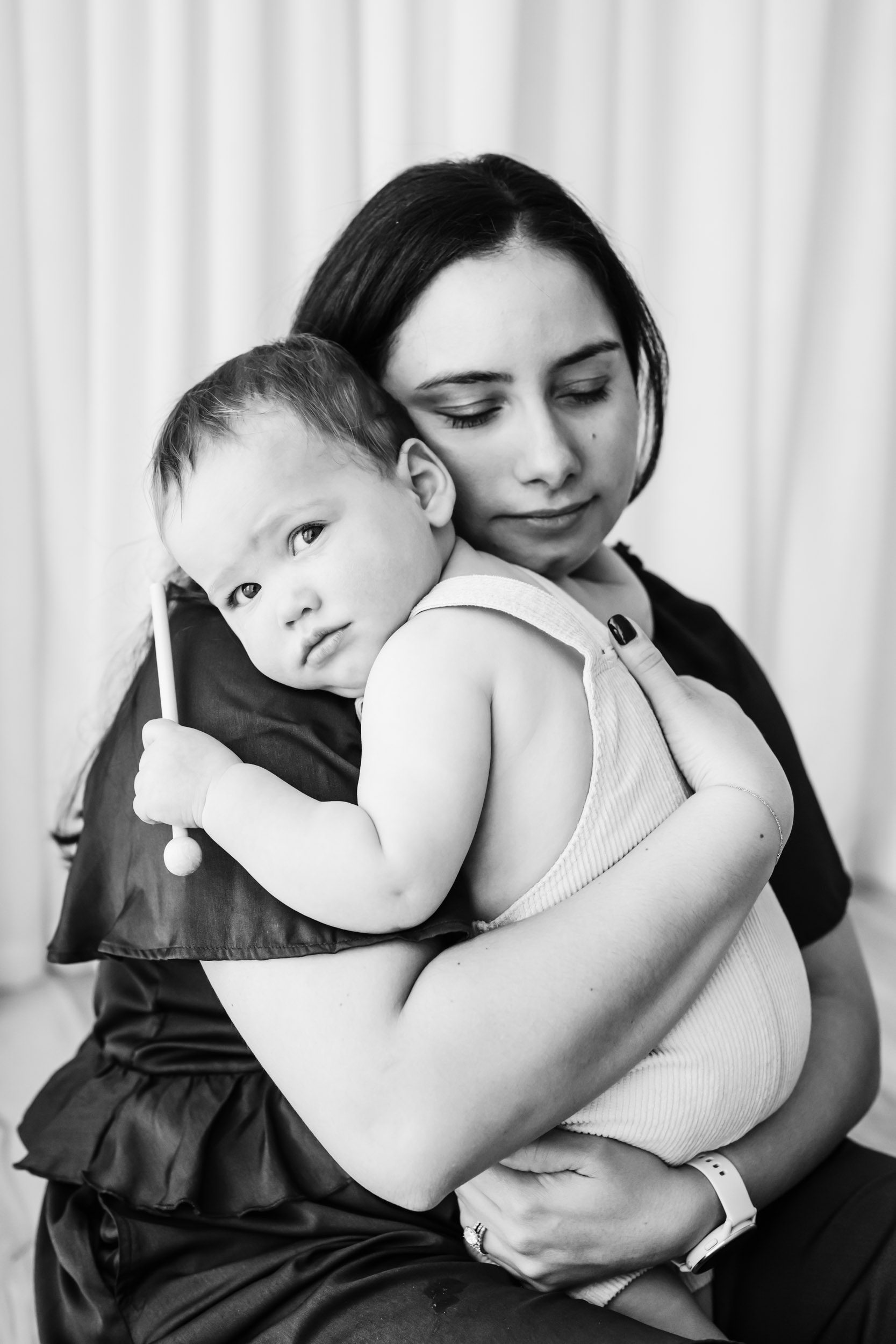 a black and white picture of a mom hugging her baby boy as he gazes at the camera over her shoulder during a Mommy & Me photoshoot