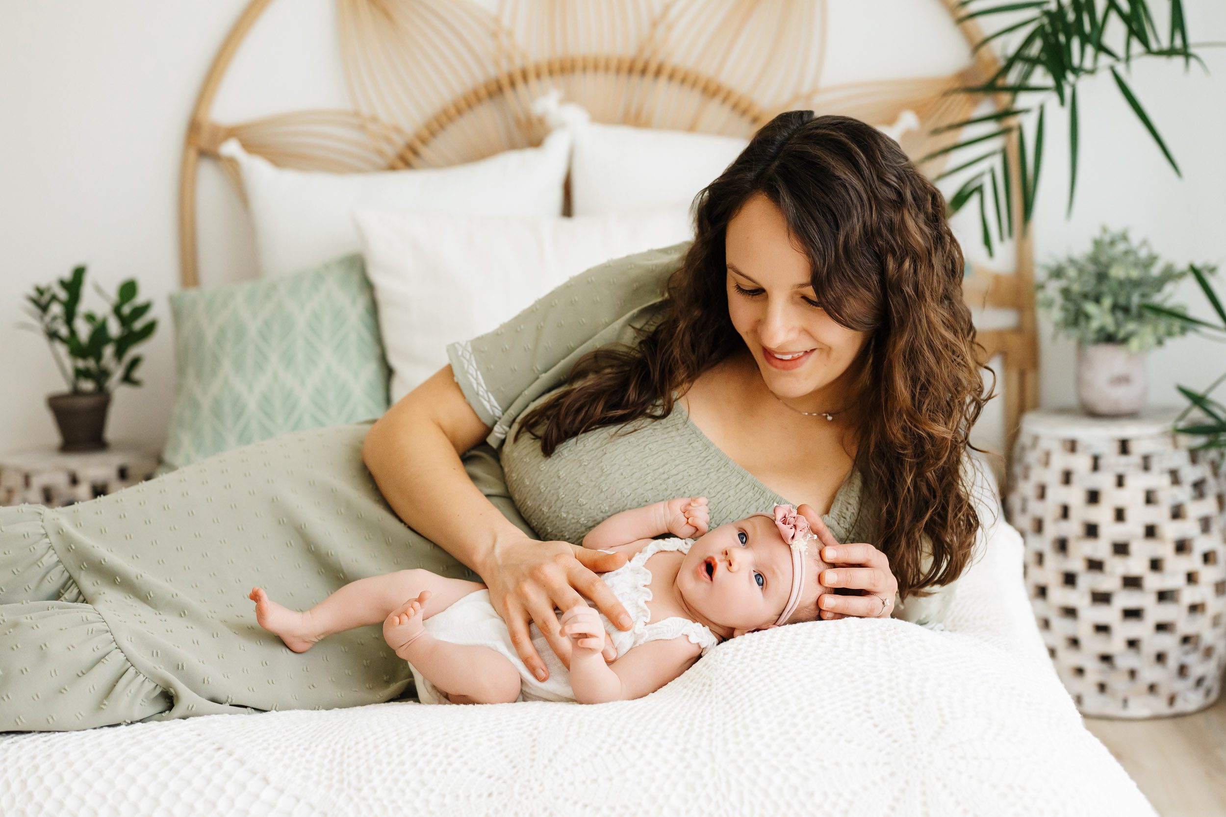 a new mother laying on a bed with her baby girl and smiling down at her during a Schwenksville newborn photography session